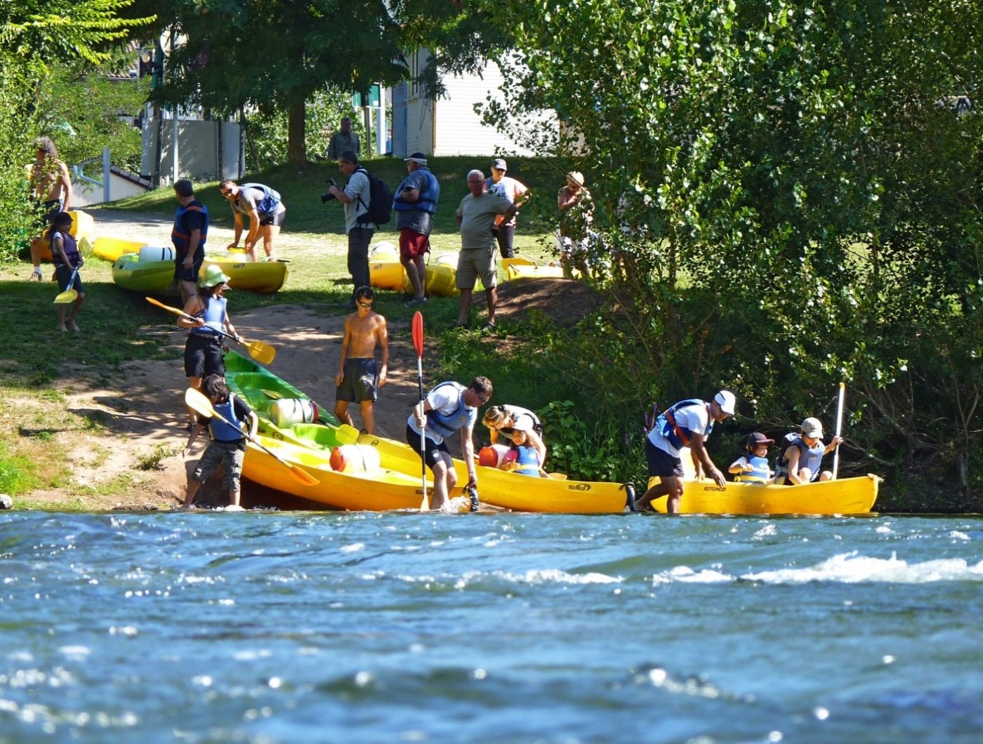 Passionnés de canoë-kayak se préparant à naviguer sur la rivière Tarn, avec des kayaks jaunes prêts à partir pour une aventure en eau vive, sous le soleil d'été, offrant une activité populaire pour les visiteurs de l'Hostellerie des Lauriers.