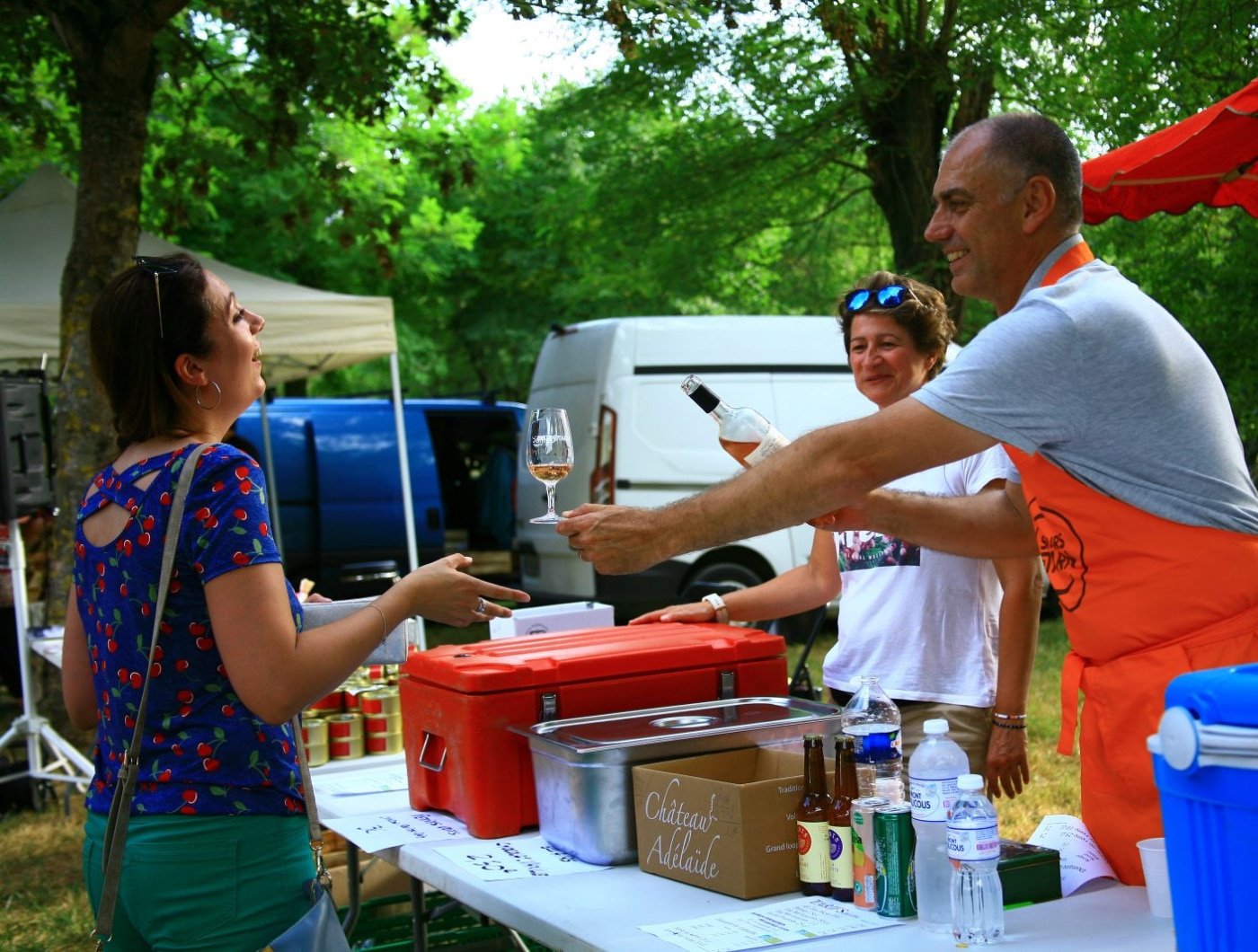 Pascal Sudre accueille chaleureusement les visiteurs au stand de l'Hostellerie des Lauriers lors du marché de Villeneuve-sur-Tarn, présentant des produits locaux et partageant un moment convivial autour d'une dégustation de vin.