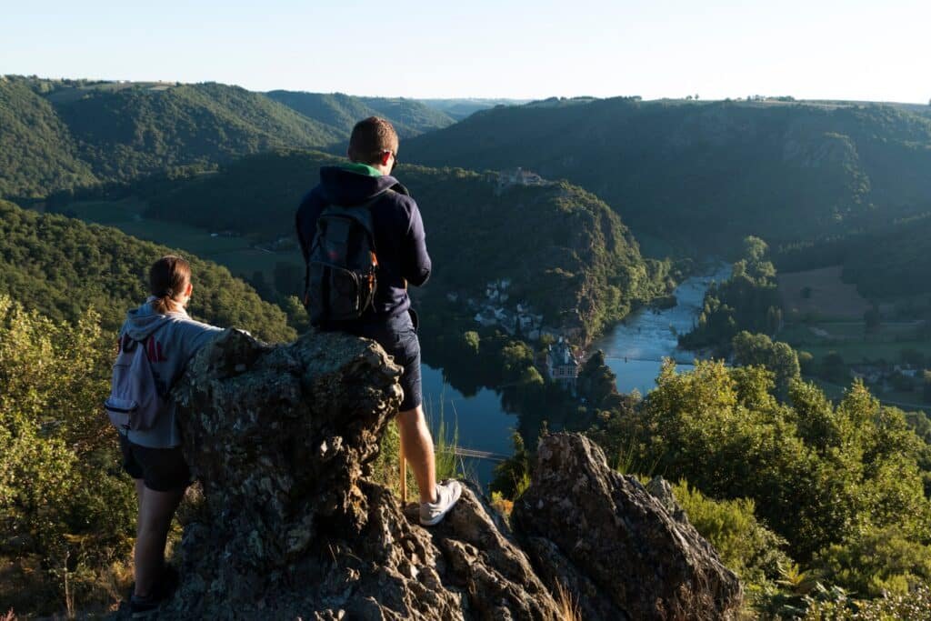 "Deux randonneurs profitent d'une vue imprenable sur le méandre d'Ambialet au lever du soleil, reflétant la tranquillité et la beauté naturelle que les visiteurs peuvent découvrir près de l'Hostellerie des Lauriers.