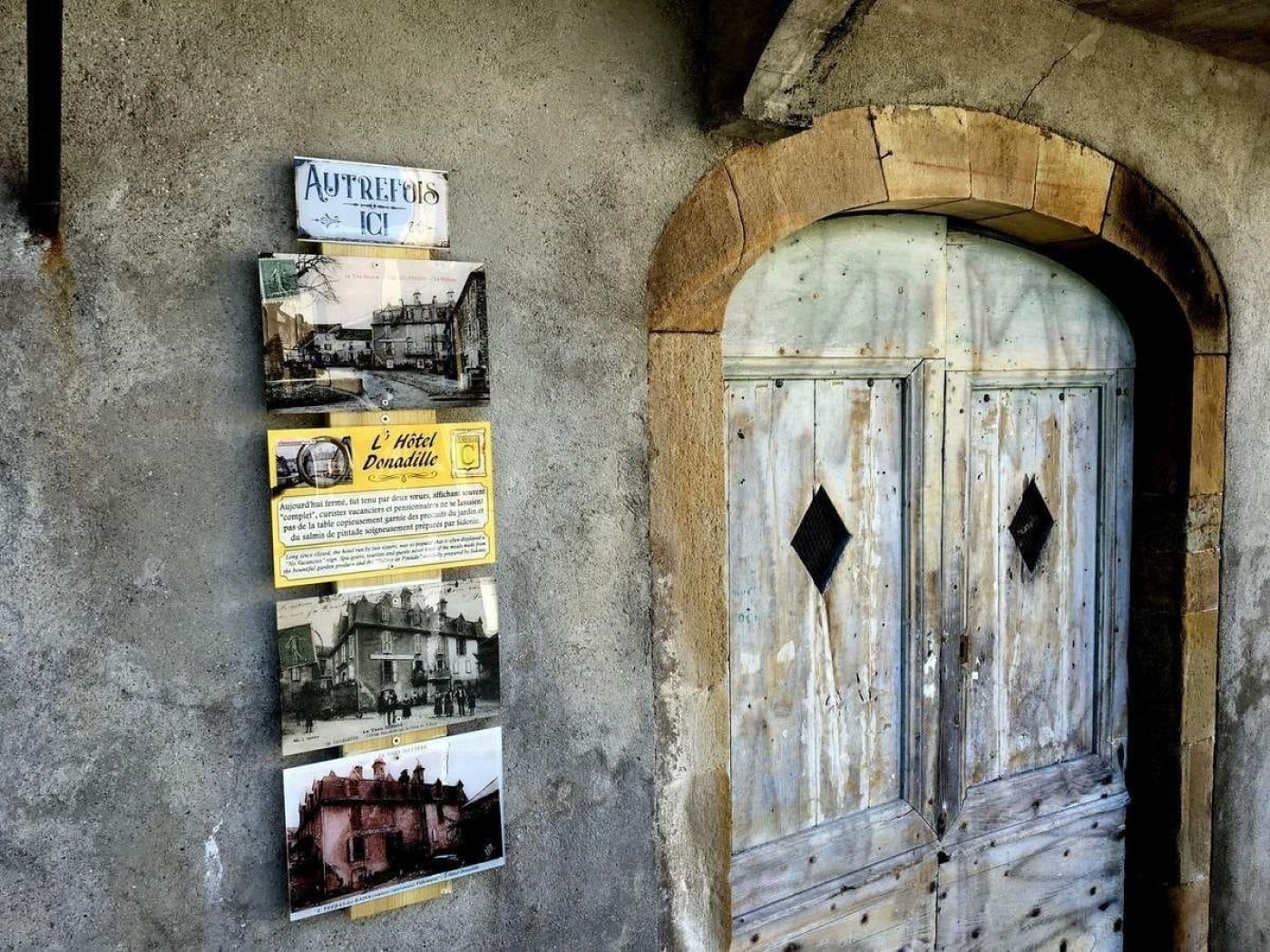 Totem historique affichant l'évolution de Villeneuve-sur-Tarn juxtaposés à une porte en bois ancienne, offrant un aperçu du riche patrimoine et de l'histoire captivante du village à l'Hostellerie des Lauriers.