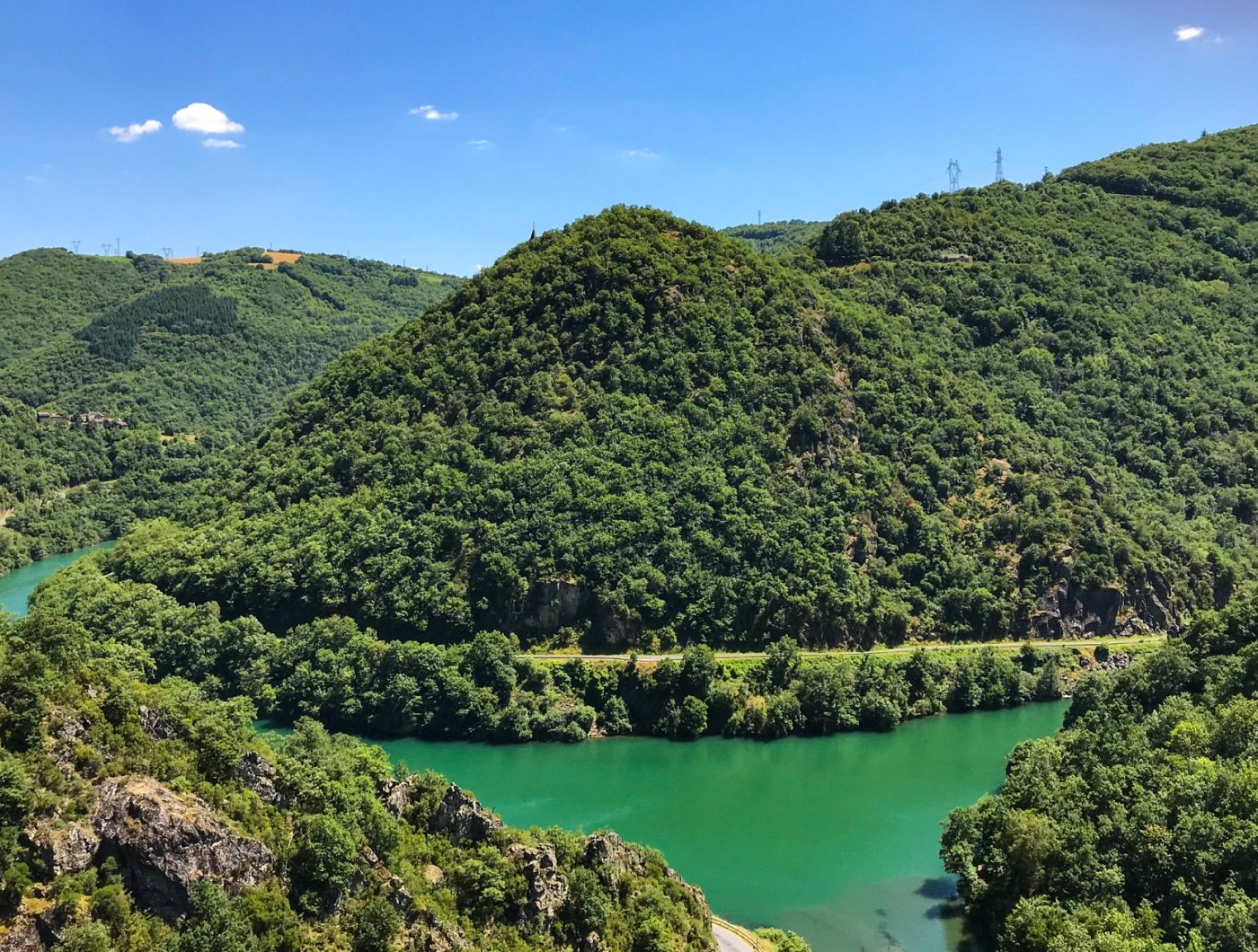 La Vallée du Tarn se dévoile sous un ciel d'été clair, avec ses collines luxuriantes et la rivière Tarn serpentine d'un vert émeraude, capturant la beauté naturelle et paisible près de l'Hostellerie des Lauriers.